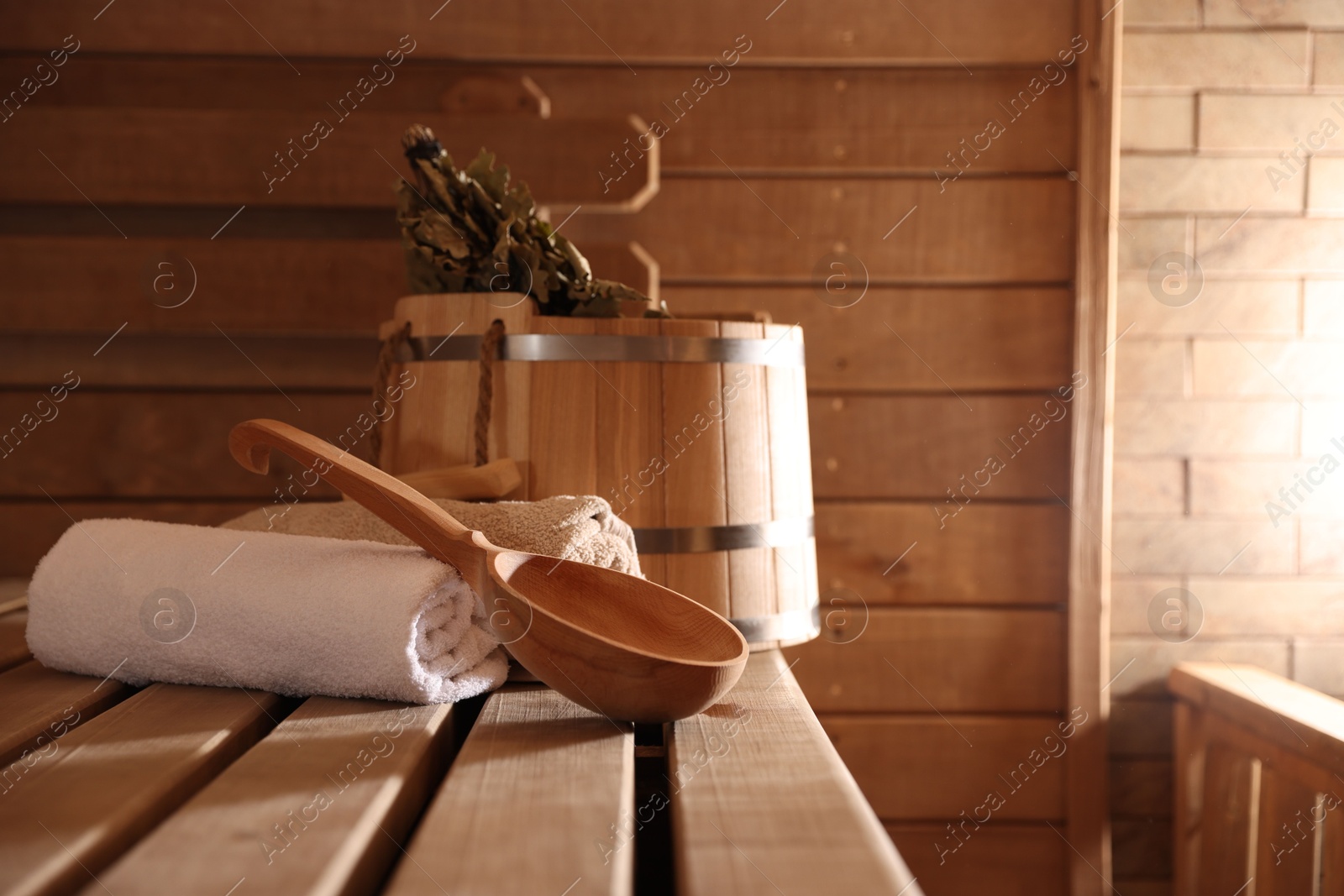 Photo of Ladle, towels, bucket and whisk on wooden bench in sauna. Space for text