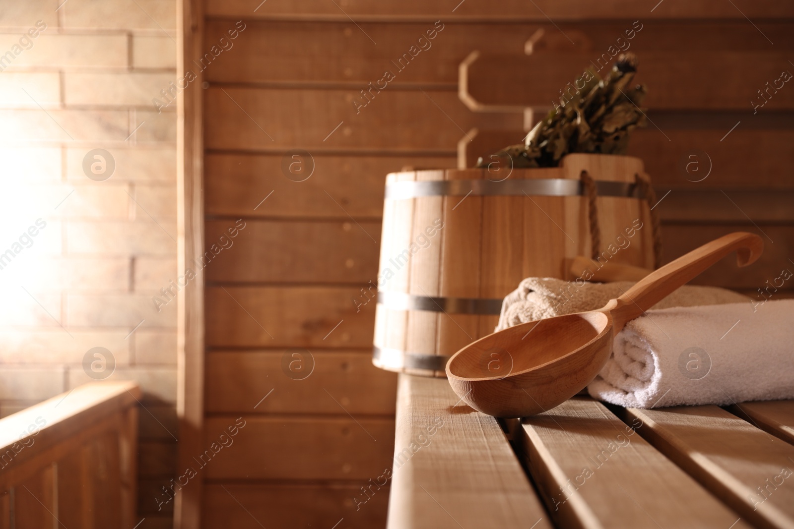 Photo of Ladle, towels, bucket and whisk on wooden bench in sauna. Space for text