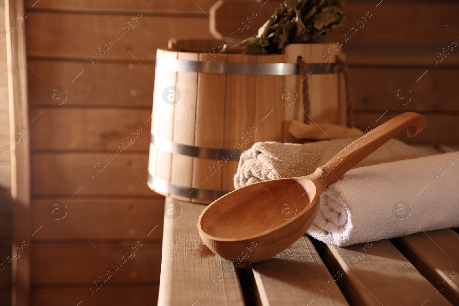 Photo of Ladle, towels, bucket and whisk on wooden bench in sauna. Space for text