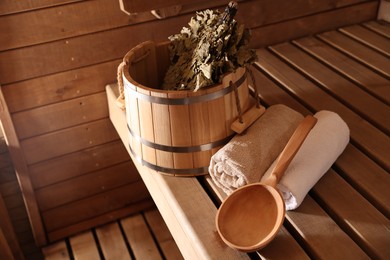 Photo of Bucket, whisk and towels on wooden bench in sauna. Space for text