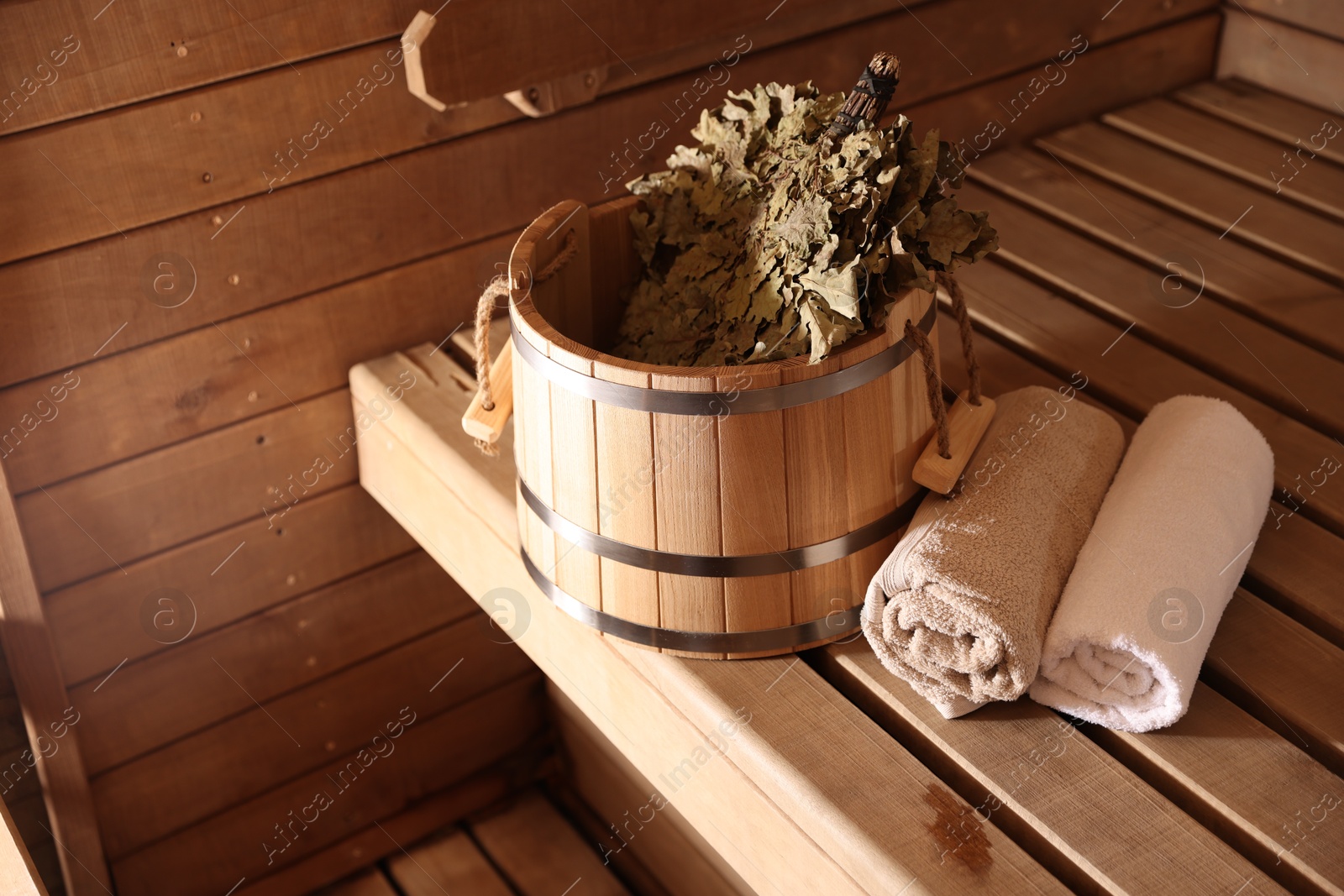 Photo of Bucket, whisk and towels on wooden bench in sauna. Space for text