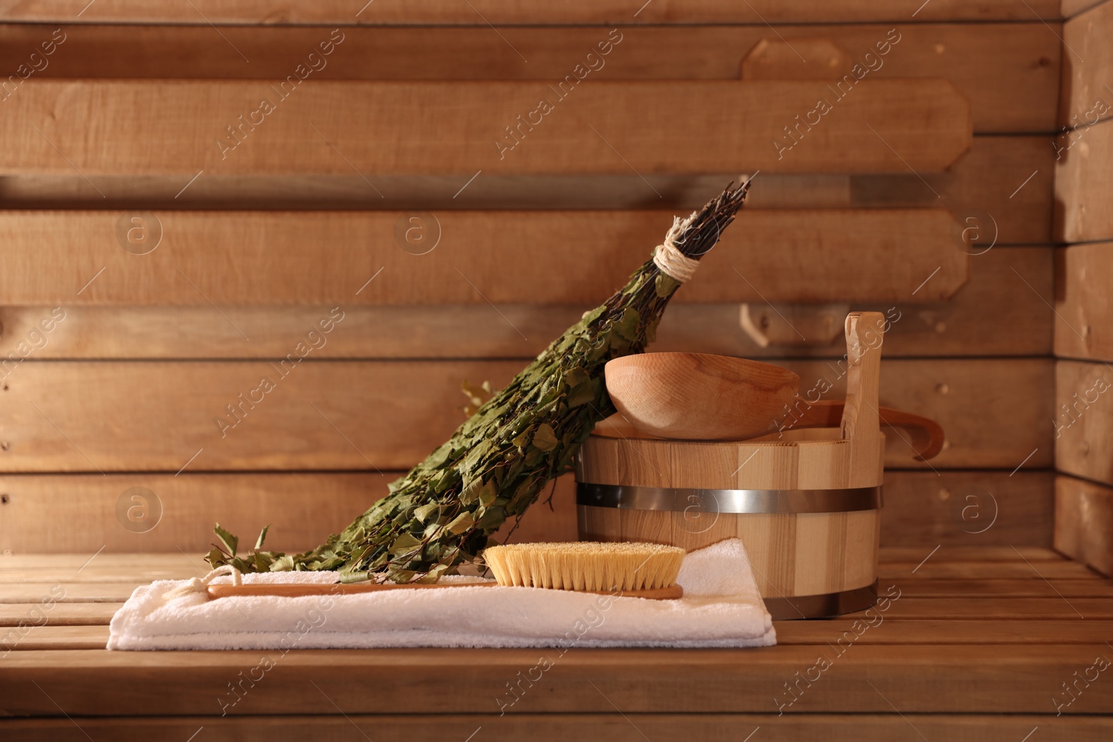 Photo of Massaging brush, towel, bucket, whisk and ladle on wooden bench in sauna