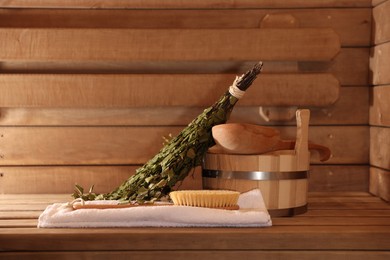 Photo of Massaging brush, towel, bucket, whisk and ladle on wooden bench in sauna