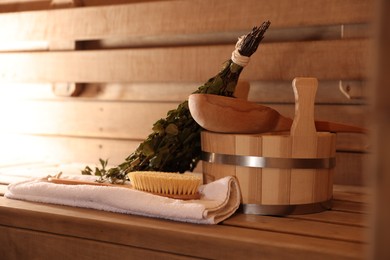 Photo of Massaging brush, towel, bucket, whisk and ladle on wooden bench in sauna