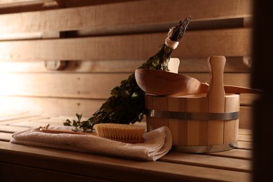 Photo of Massaging brush, towel, bucket, whisk and ladle on wooden bench in sauna