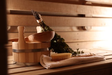 Photo of Massaging brush, towel, bucket, whisk and ladle on wooden bench in sauna