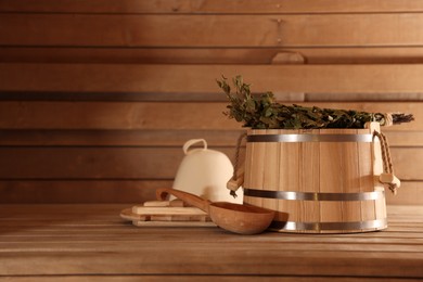 Photo of Bucket, ladle and whisk on wooden bench in sauna. Space for text