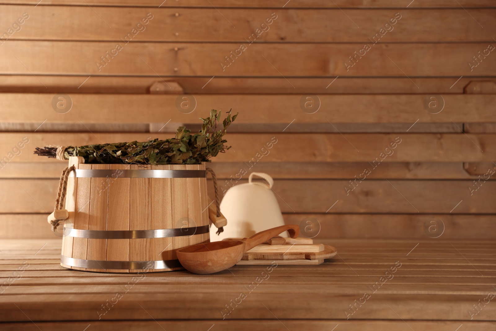 Photo of Bucket, ladle and whisk on wooden bench in sauna. Space for text