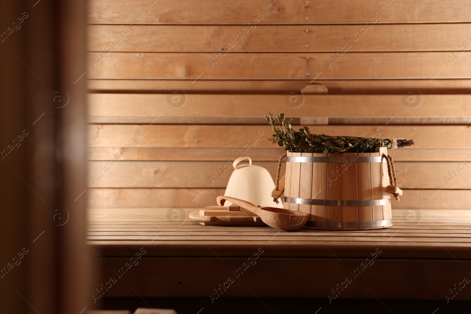 Photo of Bucket, ladle and whisk on wooden bench in sauna. Space for text