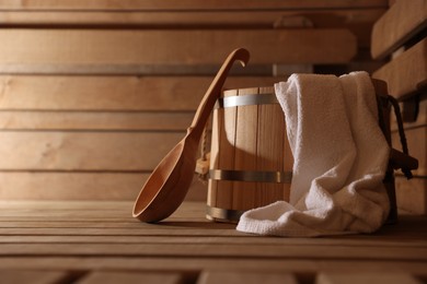 Photo of Bucket, ladle and towel on wooden bench in sauna. Space for text