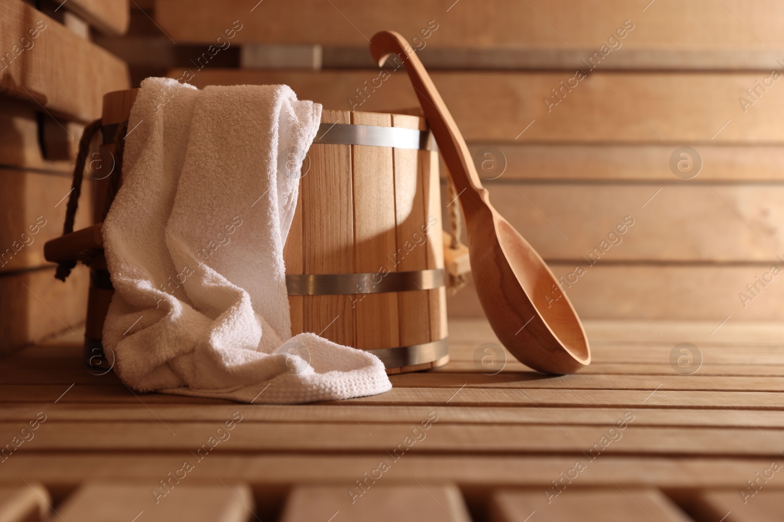 Photo of Bucket, ladle and towel on wooden bench in sauna. Space for text