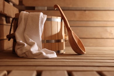 Photo of Bucket, ladle and towel on wooden bench in sauna. Space for text