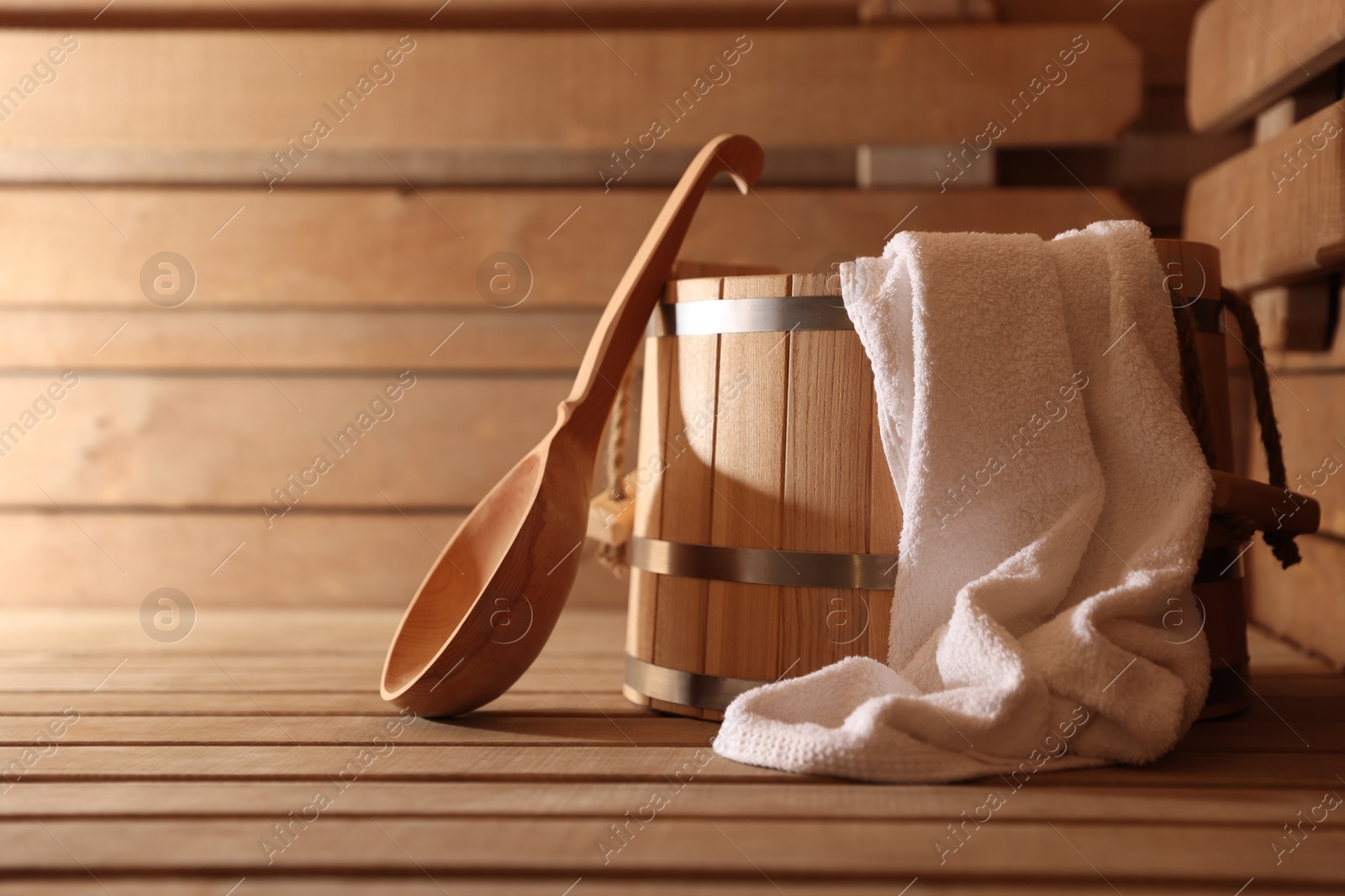 Photo of Bucket, ladle and towel on wooden bench in sauna. Space for text