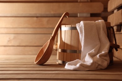 Photo of Bucket, ladle and towel on wooden bench in sauna. Space for text