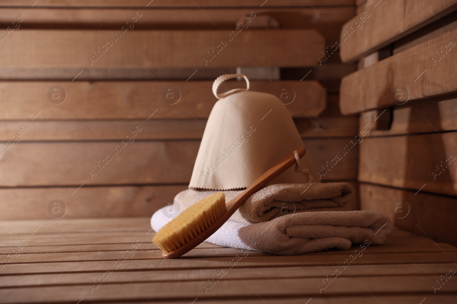 Photo of Massaging brush, hat and towels on wooden bench in sauna. Space for text