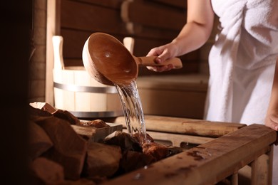 Photo of Woman pouring water onto stones in sauna, closeup