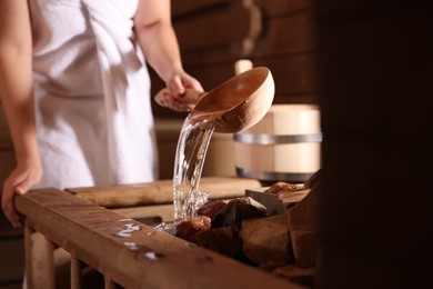 Photo of Woman pouring water onto stones in sauna, closeup