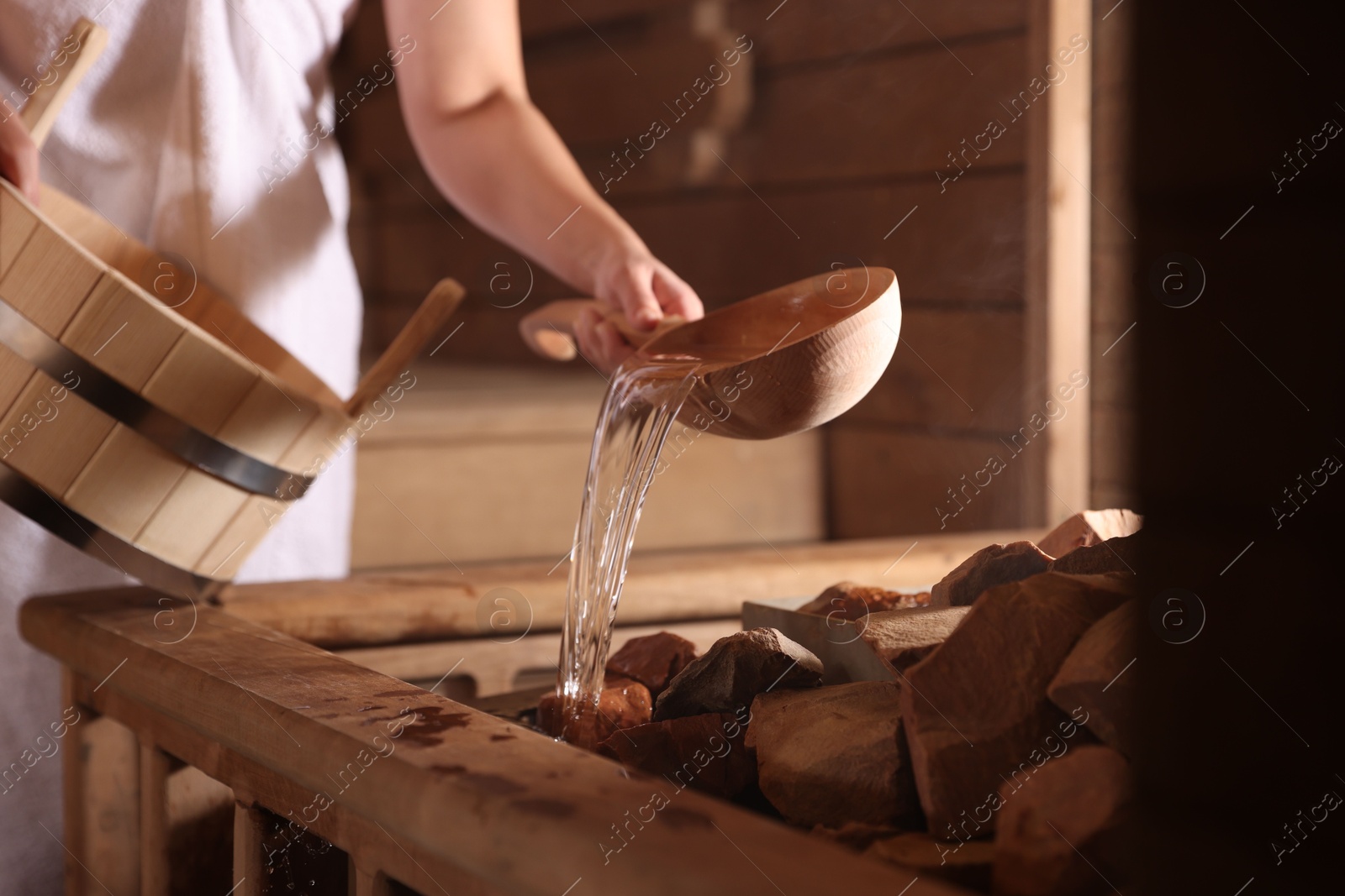 Photo of Woman pouring water onto stones in sauna, closeup