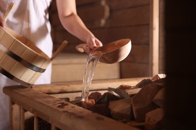 Photo of Woman pouring water onto stones in sauna, closeup