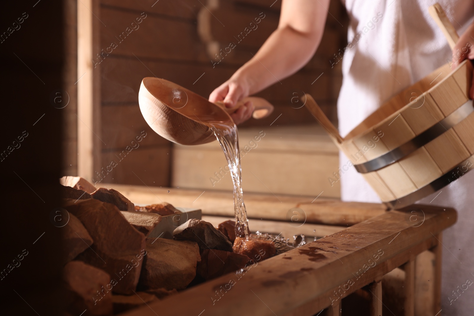 Photo of Woman pouring water onto stones in sauna, closeup