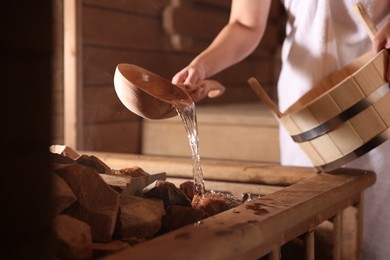 Photo of Woman pouring water onto stones in sauna, closeup