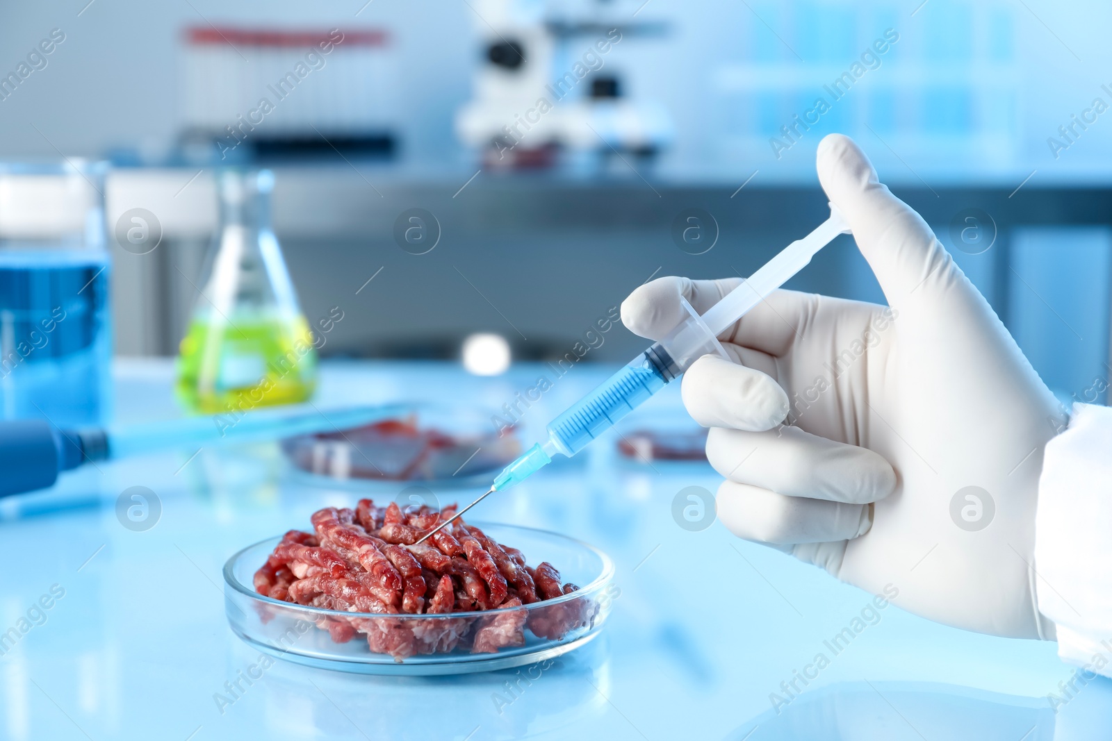 Photo of GMO concept. Scientist injecting something into minced meat at table in laboratory, closeup