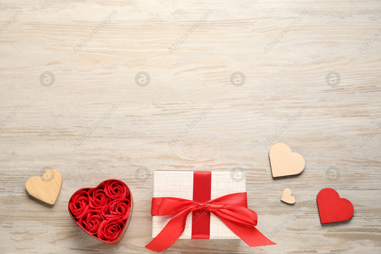 Photo of Romantic gift, roses buds and decorative hearts on light wooden table, flat lay with space for text. Happy Valentine's day