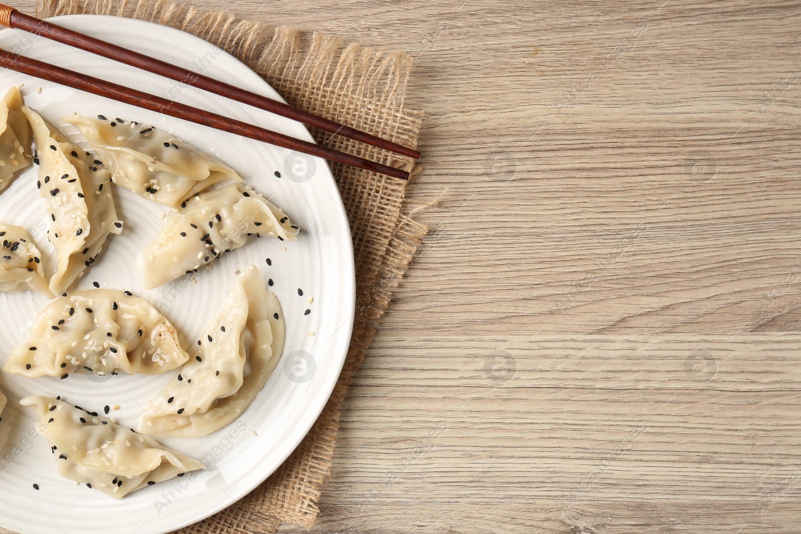 Photo of Delicious gyoza dumplings with sesame seeds served on wooden table, top view. Space for text