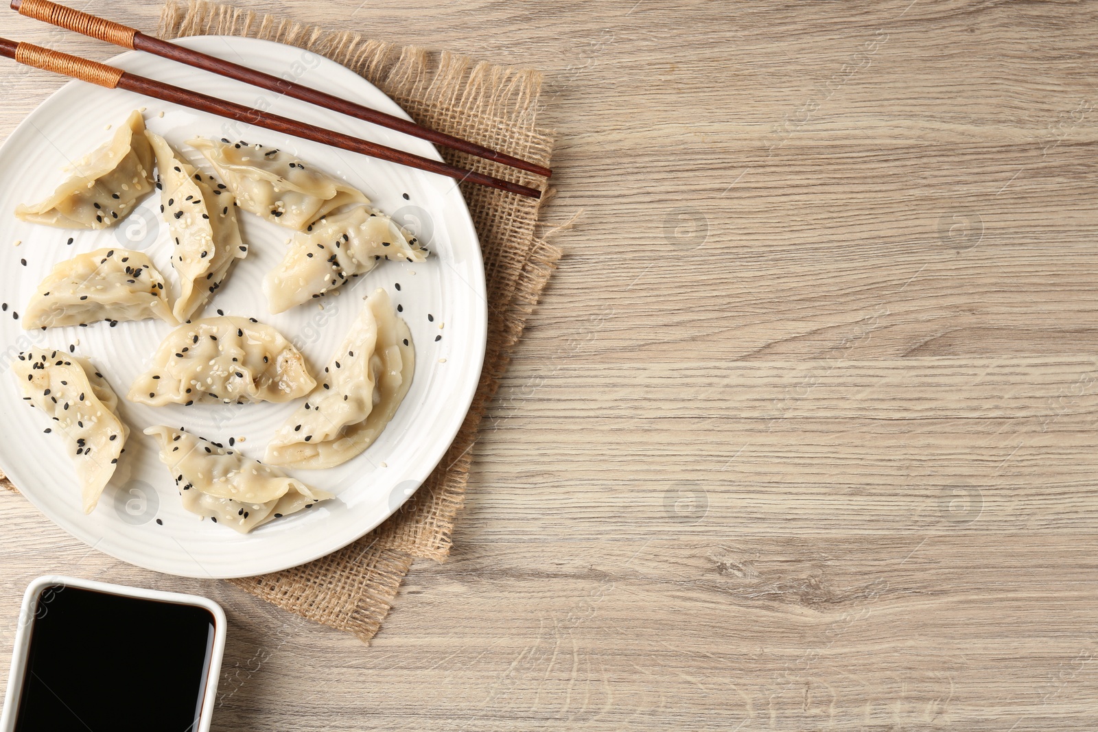 Photo of Delicious gyoza dumplings with sesame seeds served on wooden table, top view. Space for text