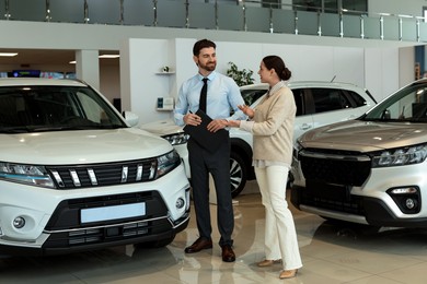 Photo of Happy salesman and client near new car in salon