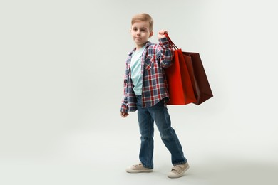 Photo of Cute little boy with shopping bags on grey background. Space for text