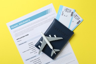 Photo of Medical tourism. Travel insurance application form, passport, flight tickets and plane model on yellow background, top view