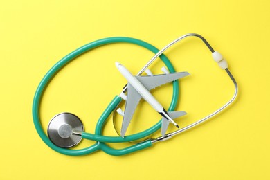 Photo of Medical tourism. Stethoscope and plane model on yellow background, flat lay