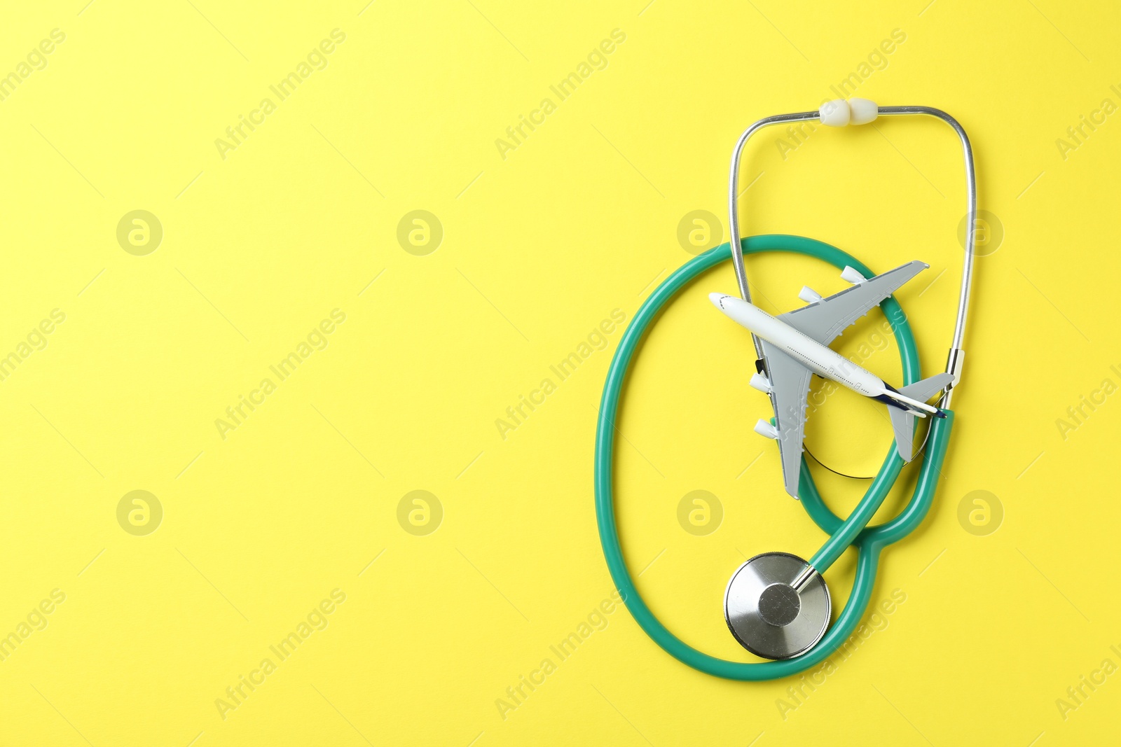 Photo of Medical tourism. Stethoscope and plane model on yellow background, flat lay. Space for text