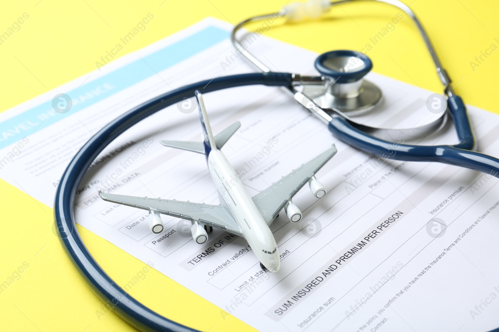 Photo of Medical tourism. Travel insurance application form, stethoscope and plane model on yellow background, closeup