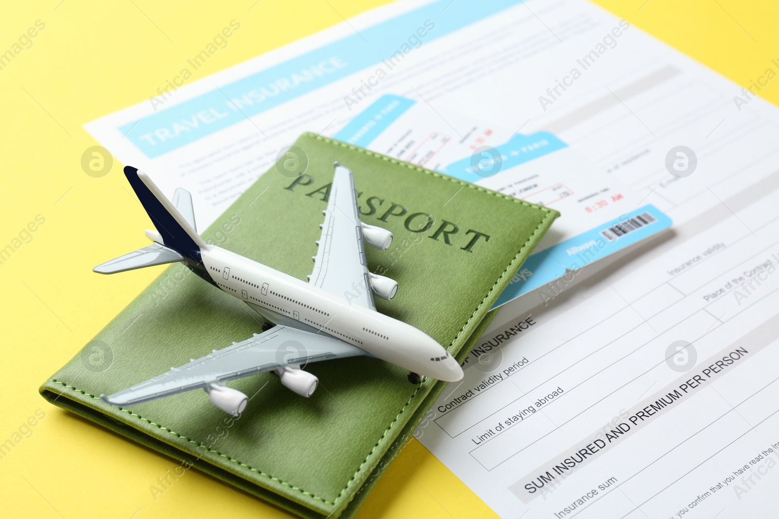 Photo of Medical tourism. Travel insurance application form, passport, flight tickets and plane model on yellow background, closeup