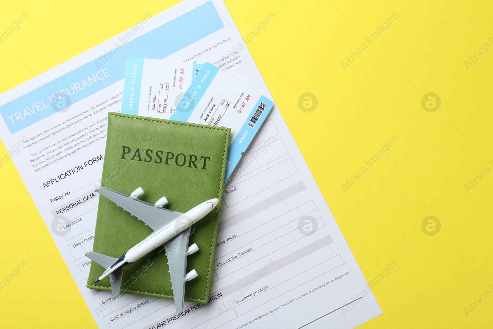 Photo of Medical tourism. Travel insurance application form, passport, flight tickets and plane model on yellow background, top view. Space for text