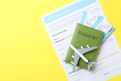 Photo of Medical tourism. Travel insurance application form, passport, flight tickets and plane model on yellow background, top view. Space for text