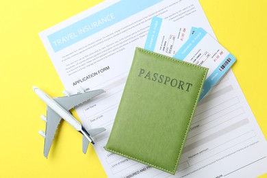 Photo of Medical tourism. Travel insurance application form, passport, flight tickets and plane model on yellow background, flat lay