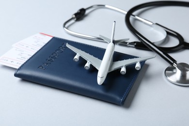 Photo of Medical tourism. Stethoscope, passport, flight tickets and plane model on light grey background, closeup