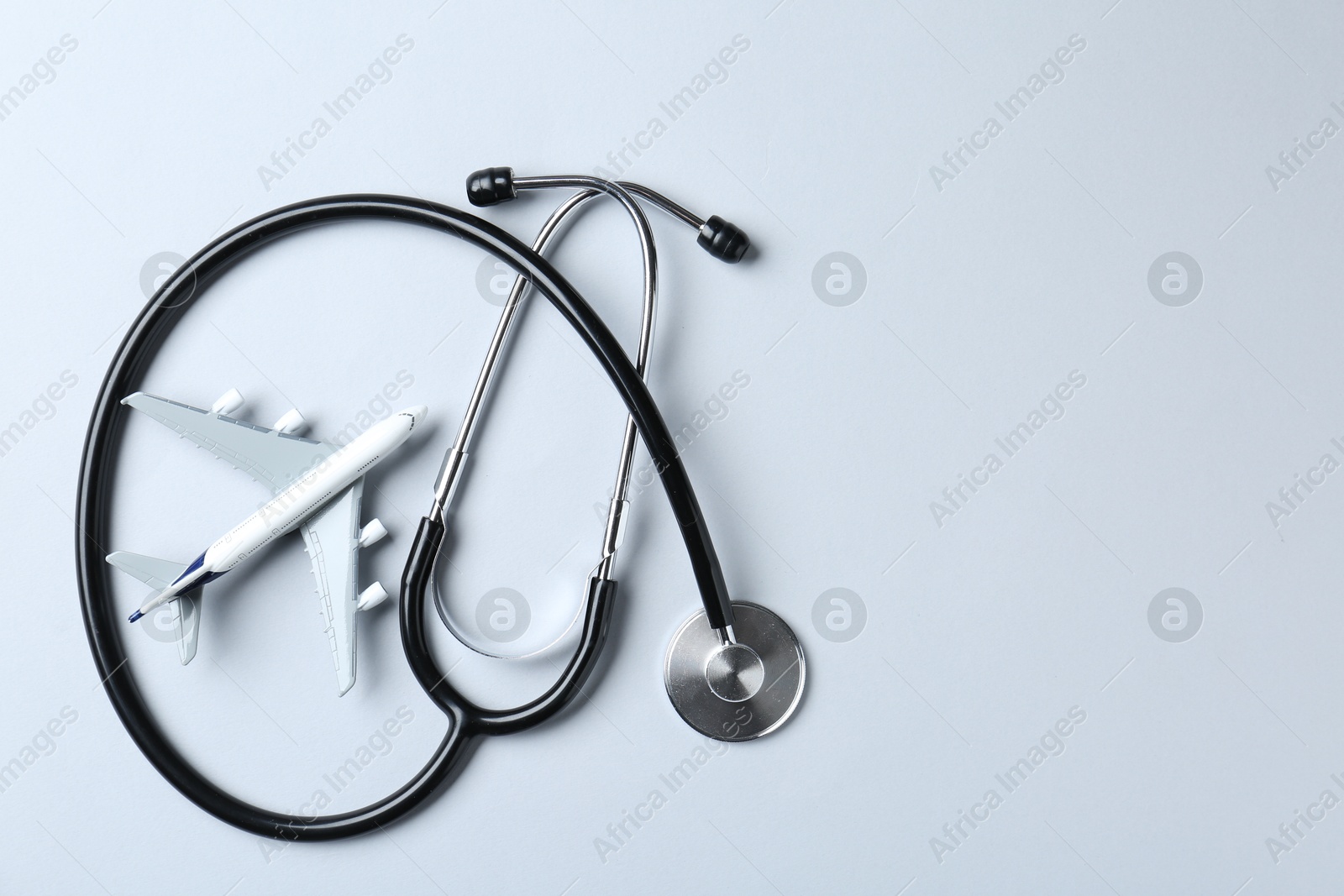 Photo of Medical tourism. Stethoscope and plane model on light grey background, flat lay. Space for text