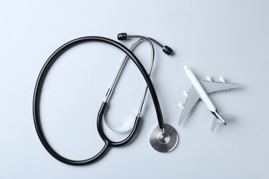 Photo of Medical tourism. Stethoscope and plane model on light grey background, flat lay