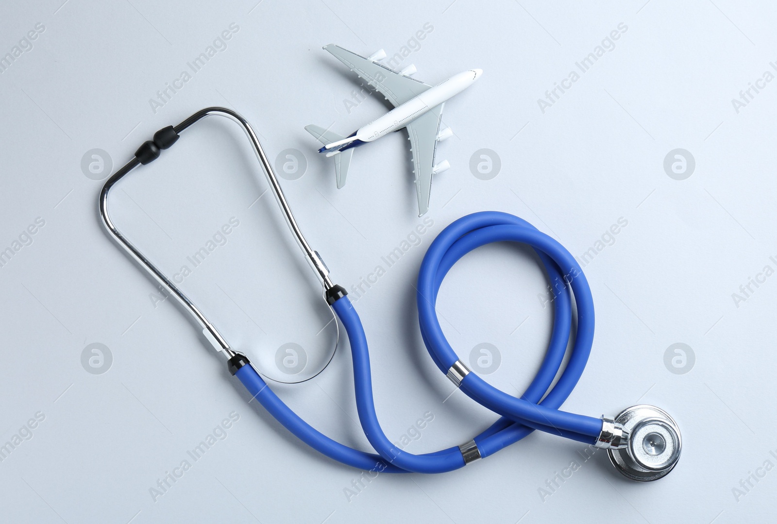 Photo of Medical tourism. Stethoscope and plane model on light grey background, flat lay