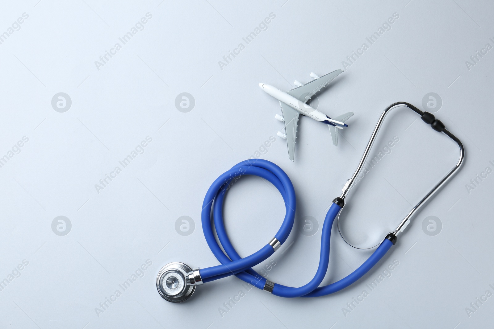 Photo of Medical tourism. Stethoscope and plane model on light grey background, flat lay. Space for text