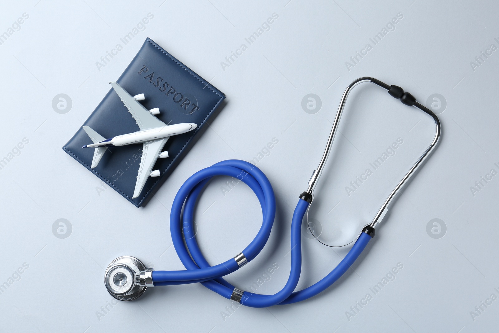 Photo of Medical tourism. Stethoscope, passport and plane model on light grey background, flat lay