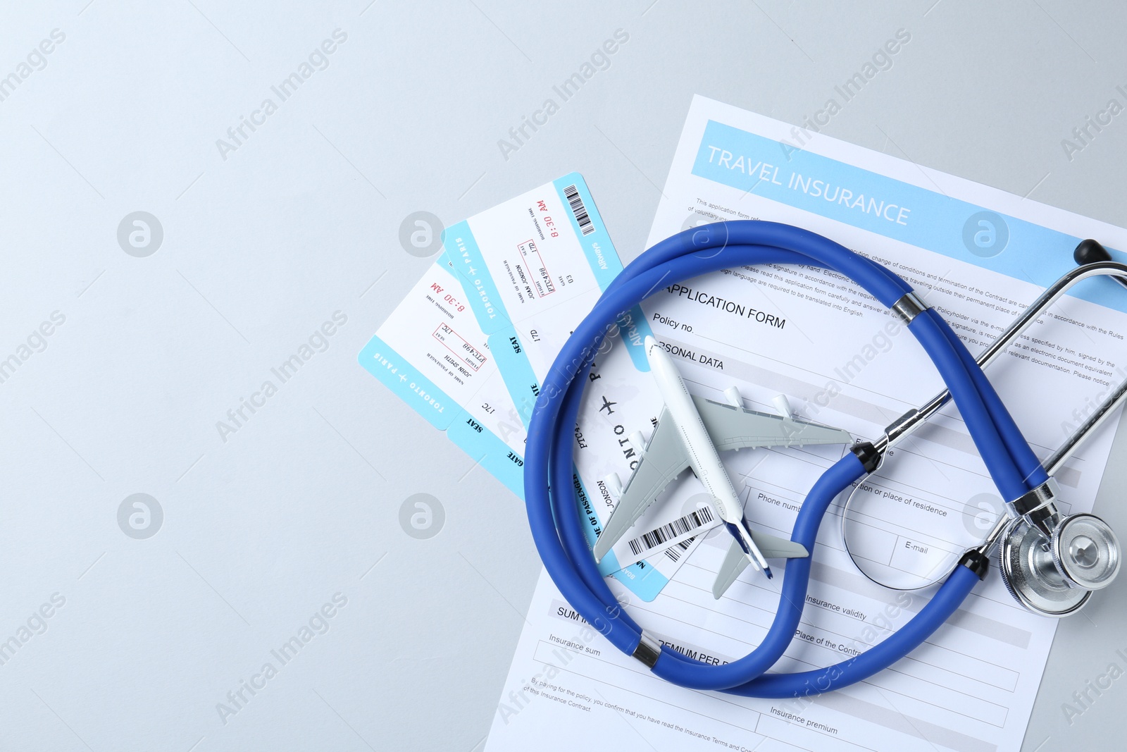 Photo of Medical tourism. Travel insurance application form, stethoscope, plane model and flight tickets on light background, flat lay. Space for text