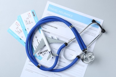 Photo of Medical tourism. Travel insurance application form, stethoscope, plane model and flight tickets on light background, flat lay