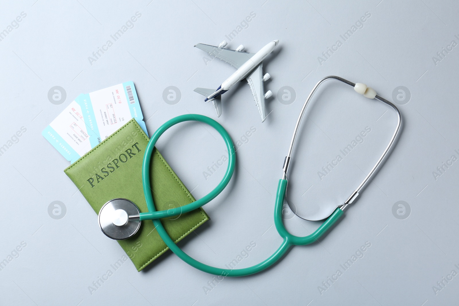 Photo of Medical tourism. Stethoscope, plane model, passport and flight tickets on light blue background, flat lay