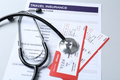 Photo of Medical tourism. Travel insurance application form, stethoscope and flight tickets on light background