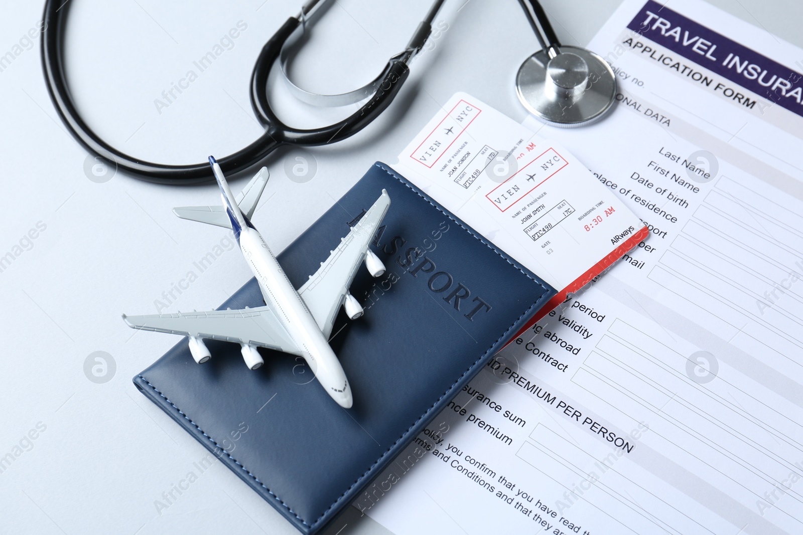 Photo of Medical tourism. Travel insurance application form, stethoscope, plane model, passport and flight tickets on light background